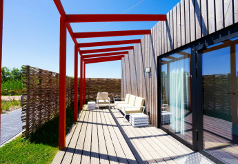 Terrasse ved Resort Callantsoog 5 i Holland med moderne stole, trædæk og røde bjælker under blå himmel.
