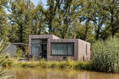 Moderne tiny house ved søen i Holiday Park Schaijk, omgivet af træer og grøn natur, set i dagslys.