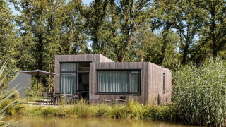 Casa diminuta moderna en Holiday Park Schaijk al lado de un lago, rodeada de árboles y naturaleza luminosa.