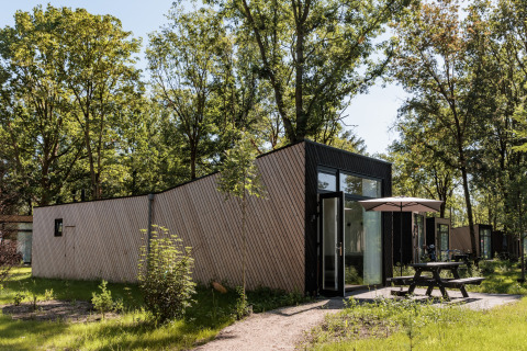 Vue extérieure de la tiny house Holiday Park Schaijk 7 avec table, parasol et arbres verdoyants alentours.