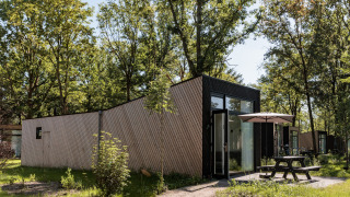 Udendørsbillede af Holiday Park Schaijk 7 tiny house med terrasse, bord og parasol omgivet af træer.