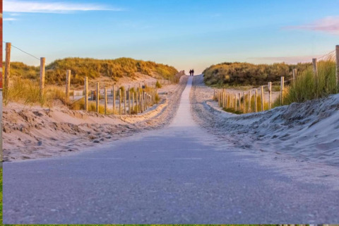 Zandweg tussen duinen met houten palen bij Resort Callantsoog 5 in Nederland onder avondlucht.