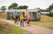 Family cycling on a path by cabins at Holiday Park Loodsmansduin 1, Netherlands, surrounded by nature.