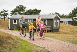 Famiglia in bicicletta davanti a case vacanza a Holiday Park Loodsmansduin 1, Paesi Bassi, nella natura.