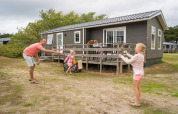 Family plays outside a wooden lodge at Holiday Park Loodsmansduin 1 in the Netherlands on a cloudy day.