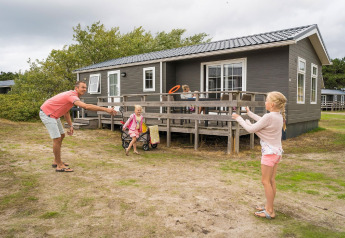 Family plays outside a wooden lodge at Holiday Park Loodsmansduin 1 in the Netherlands on a cloudy day.
