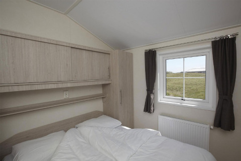 Schlafzimmer mit Doppelbett, Fenster mit Blick auf grüne Wiese, Vorhänge und Schränke im Loodsmansduin.