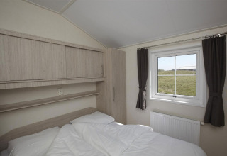Soveværelse med dobbeltseng og vindue, udsigt til grøn eng, gardiner og skabe på Holiday Park Loodsmansduin.