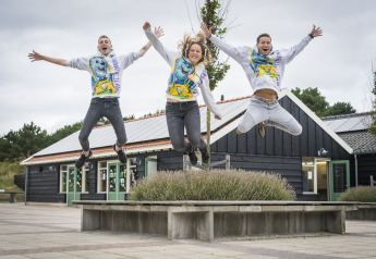 Three young people joyfully jump in front of Holiday Park Loodsmansduin 1, a lodge in the Netherlands.