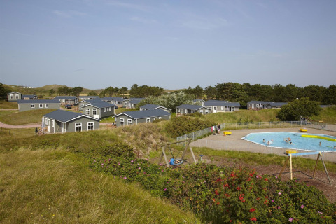 Landschaft des Ferienparks Loodsmansduin 1 in den Niederlanden mit Hütten, Pool und Spielplatz.