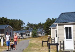 Par slentrer gennem ferielandsby Holiday Park «Loodsmansduin 1» med hytter i solrigt landskab, Holland.