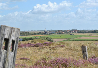 Scenic view from Holiday Park Loodsmansduin 1 with purple heath, fields, and a church in the Dutch village.