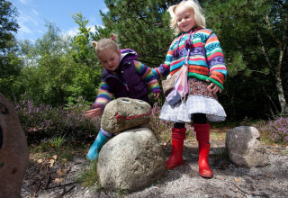 Deux enfants jouent dehors en pulls colorés auprès de pierres décorées au Holiday Park Loodsmansduin, Pays-Bas.