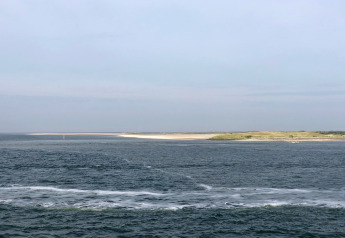 View of the sea and coastline from Holiday Park «Loodsmansduin 1» in the Netherlands under a cloudy sky.