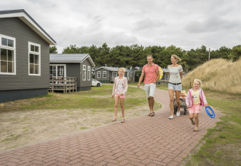 A family walks along a path at Holiday Park «Loodsmansduin 1» in the Netherlands, surrounded by cabins.