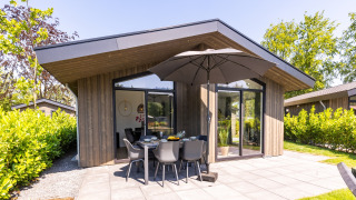 Modern chalet in Holiday Park Molenvelden 8 met terras, tuinmeubels en parasol te midden van groene natuur.