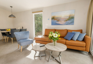 Moderne woonkamer in Holiday Park Kijkduin 9, Nederland, met lederen zetel, blauwe stoel en bloemen.