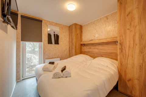 Chambre au Holiday Park 'Kijkduin 9' aux Pays-Bas avec lit double, armoires en bois et serviettes roulées.