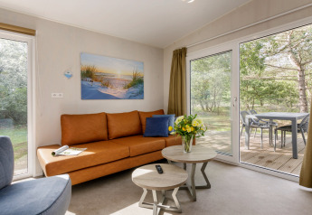 Modernes Wohnzimmer im Holiday Park «Kijkduin 9» in den Niederlanden mit braunem Sofa und Terrassenblick.