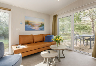 Moderne stue i Holiday Park «Kijkduin 9» i Holland med brun sofa, store vinduer og terrasseudsigt.