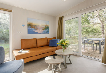 Modern living room in Holiday Park «Kijkduin 9», Netherlands, with brown sofa, big windows, and garden view.