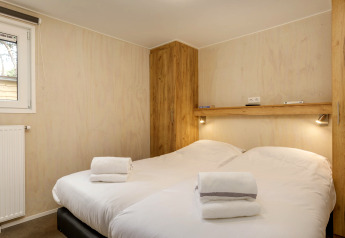 Schlafzimmer mit zwei Einzelbetten, weißen Bettlaken, Handtüchern, Holzschränken und Wandlampen im Holiday Park Kijkduin 9.