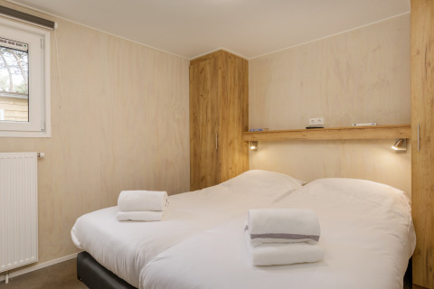 Camera da letto con due letti, lenzuola bianche, asciugamani piegati, armadi in legno e luci a parete al Holiday Park Kijkduin 9.