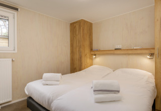 Bedroom with two beds, white linens, folded towels, wooden wardrobes, and wall lamps at Holiday Park Kijkduin 9.