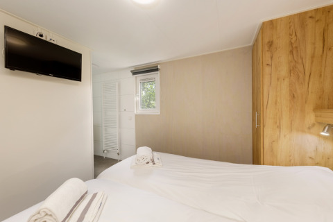 Helles Schlafzimmer im Holiday Park Kijkduin 9, Niederlande, mit zwei Betten, TV, Schrank und Bad.