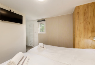 Lyst soveværelse i Holiday Park Kijkduin 9, Holland, med to senge, TV, skab og badeværelse.