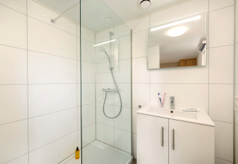 Modernes Badezimmer mit Glasdusche, weißem Waschtisch und Spiegel im Holiday Park «Kijkduin 9», Niederlande.