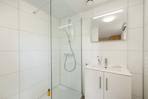 Modern bathroom with glass shower, white sink cabinet and mirror at Holiday Park «Kijkduin 9», Netherlands.