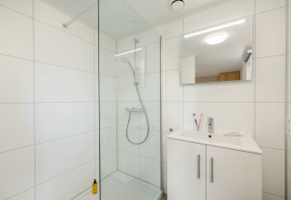 Moderne badeværelse med glasbrusekabine, hvidt skab og spejl på Holiday Park «Kijkduin 9», Holland.