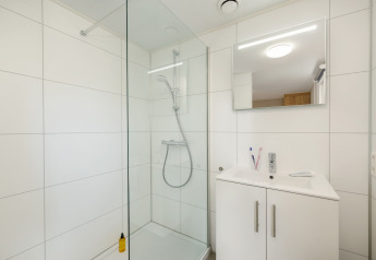 Modern bathroom with glass shower, white sink cabinet and mirror at Holiday Park «Kijkduin 9», Netherlands.