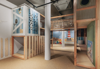 Innen-Spielplatz in einer Lodge mit Holzkonstruktionen, Kletterwand und maritimer Dekoration.