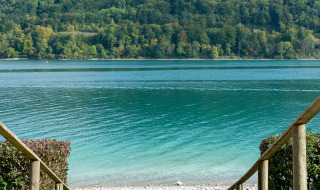 Escalera hacia una playa de guijarros y lago azul, con colinas verdes cerca de Les Abrets, Auvergne-Rhône-Alpes.
