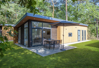 Lodge moderno en Forest Park 't Wolfsven 9 con ventanales, terraza, sombrilla y rodeado de árboles del bosque.