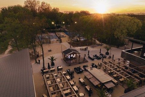 Buitenruimte van een lodge met zitjes, tafels, podium en bomen gefotografeerd bij zonsondergang.