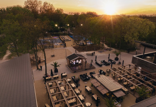 Outdoor lodge area with seating, tables, a stage, and trees captured at sunset with warm lighting.