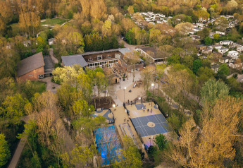 Vista aerea di un lodge tra gli alberi, con campi sportivi e piccoli edifici vicini al tramonto.