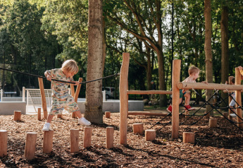 Children playing on an outdoor playground with wooden stepping posts and climbing frames at a forest lodge.