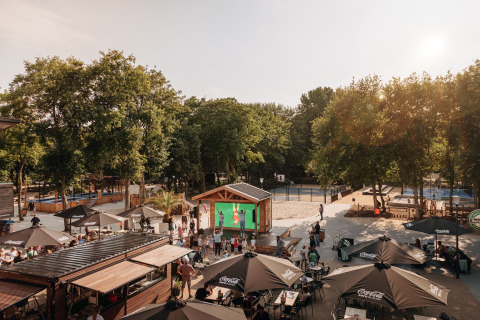 Udendørs loungeområde på Holiday Park «Kijkduin 9» i Holland med gæster, parasoller og grønne træer.