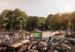 Espace extérieur du Holiday Park « Kijkduin 9 » aux Pays-Bas avec parasols, invités et beaucoup de verdure.