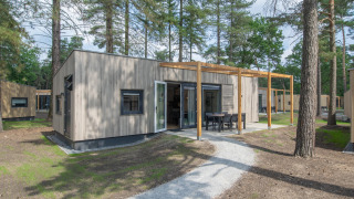 Cabaña moderna de madera en Forest Park 't Wolfsven 20, rodeada de árboles y terraza con muebles de exterior.
