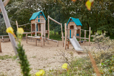 Legeplads med sand, træhuse og rutsjebane ved Holiday Park «Kijkduin 9» i Holland, omgivet af natur.