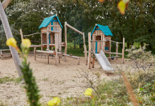 Parco giochi con sabbia, casette di legno e scivolo al Holiday Park «Kijkduin 9», Paesi Bassi, immerso nel verde.