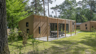 Contemporary wooden lodge at Forest Park 't Wolfsven 16, featuring a terrace with outdoor seating in nature.