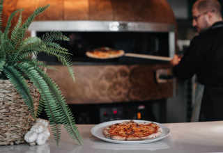 Een chef bakt pizza in een steenoven in een lodge, met een varenplant en look op de toog.