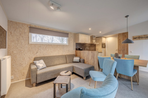 Sala y comedor modernos en Holiday Park «Kijkduin 1», Países Bajos, con sofá gris y sillas azules.