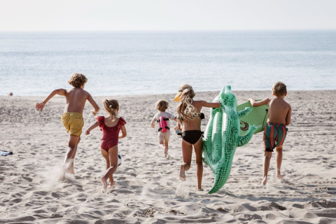 Children running on the sandy beach at Holiday Park “Kijkduin 9” in the Netherlands with an inflatable crocodile.